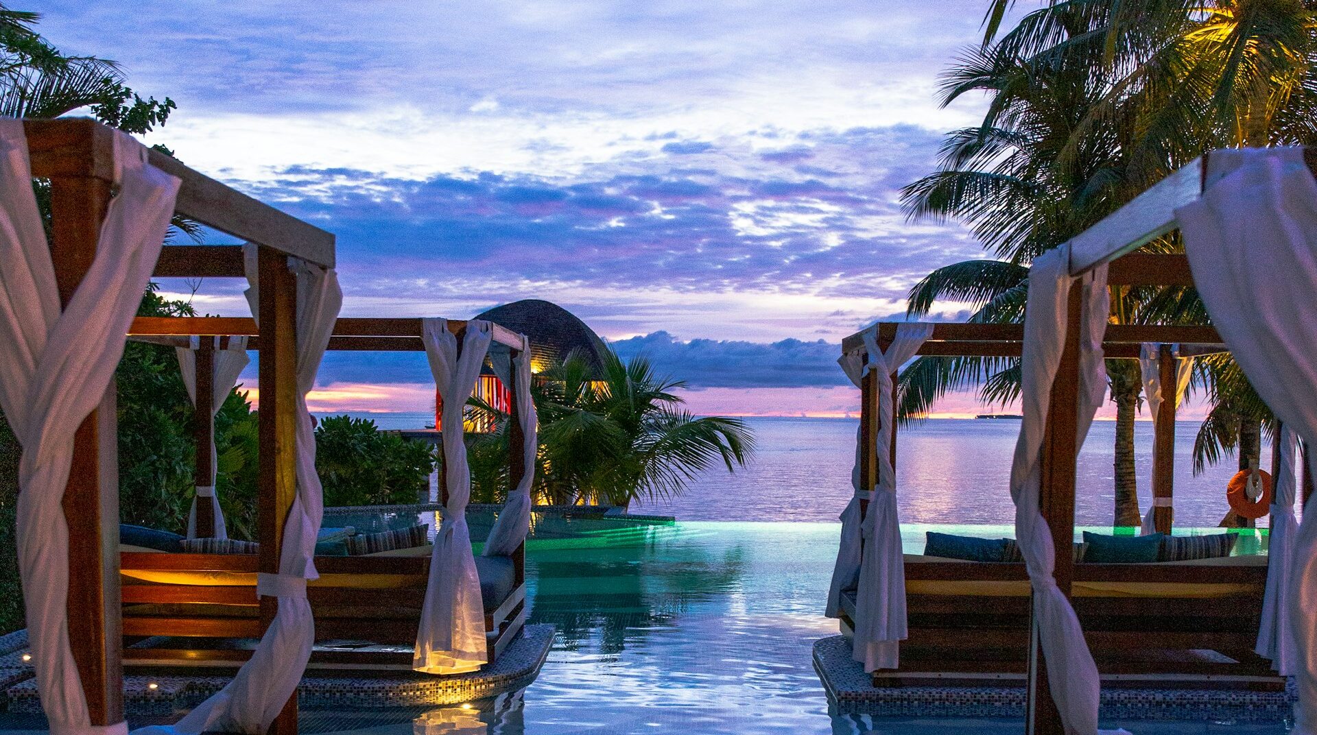 Lujosas cabañas privadas en una piscina infinita frente al océano al atardecer, representando el diseño de nuestros viajes exclusivos a la medida.